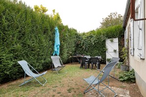 A backyard with a table and chairs, a blue umbrella, and a hedge.