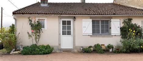 A single-story house with a tiled roof, a white door, and a window with shutters.