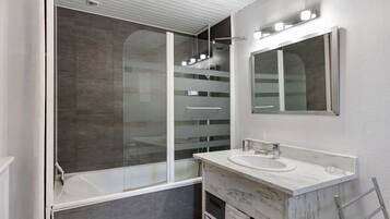 Ein modernes Badezimmer mit einer gläsernen Duschkabine, einem weißen Waschbecken mit Marmorplatte und einem Spiegel darüber.