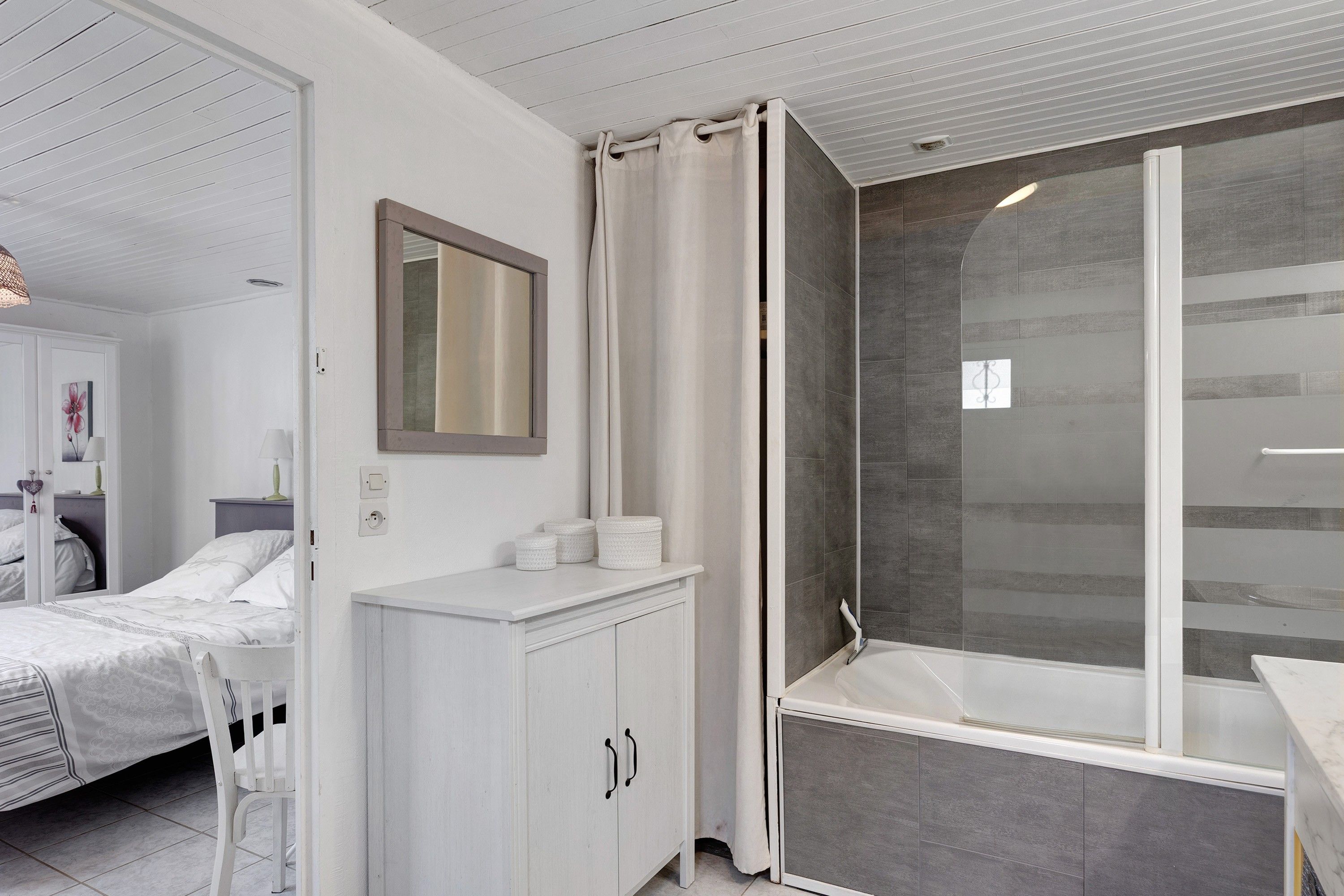 Een moderne badkamer met een douche, een wastafel en een bed in de aangrenzende kamer.
