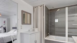A modern bathroom with a shower, a vanity, and a bed in the adjacent room.