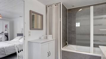 Een moderne badkamer met een douche, een wastafel en een bed in de aangrenzende kamer.