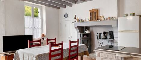 A cozy kitchen with a dining table, chairs, a television, and a stove.