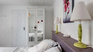A bedroom with a bed, a wardrobe, a bedside table with a lamp, and a wall with a floral painting.