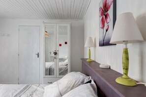 A bedroom with a bed, a wardrobe, a bedside table with a lamp, and a wall with a floral painting.