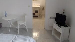 Ein Hotelzimmer mit Bett, einem kleinen runden Tisch mit einer Vase, einem weißen Stuhl, einem Fernseher auf einem Schrank und einem durch eine offene Tür sichtbaren Badezimmer.