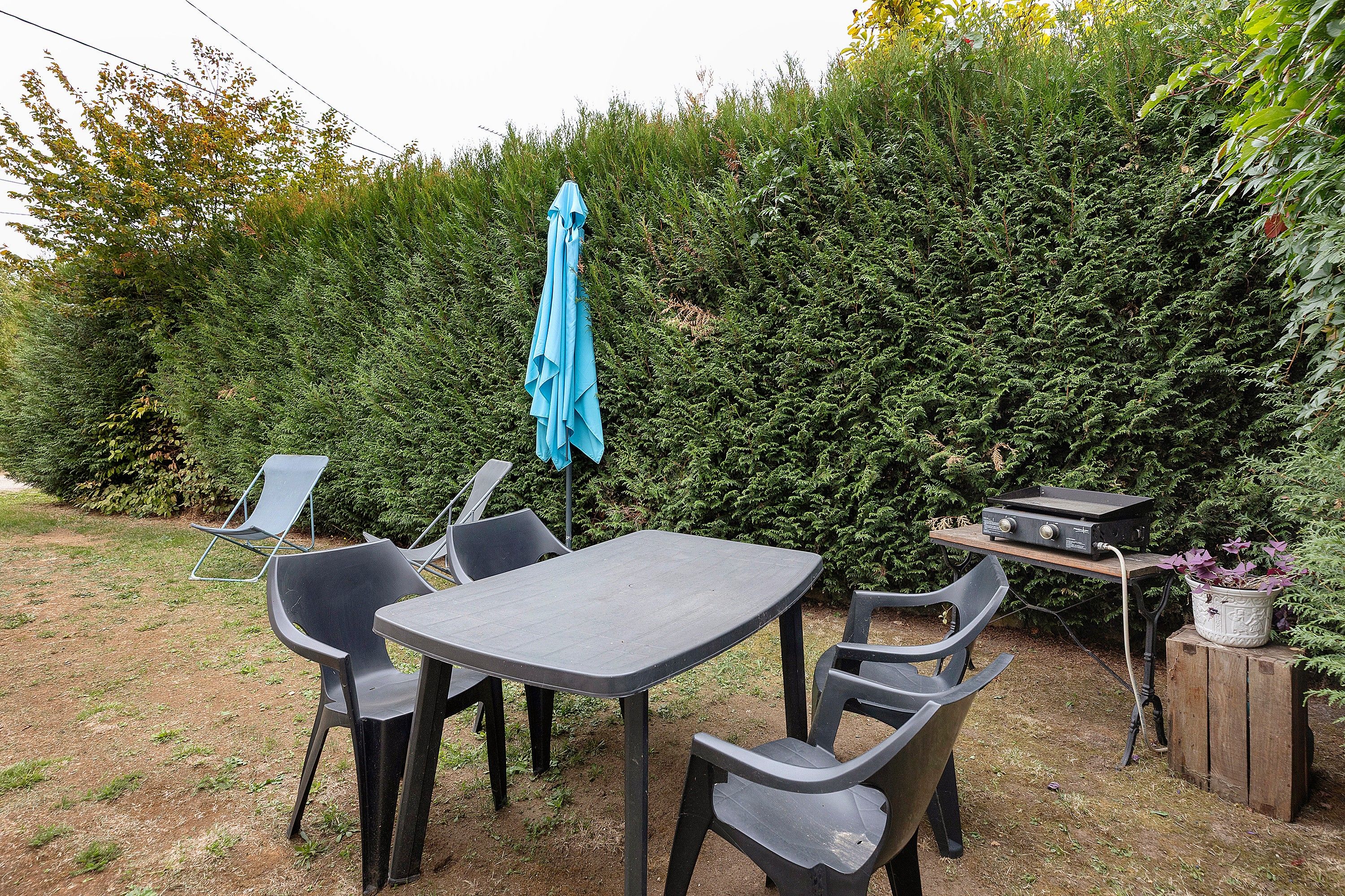 Een terras buiten met een tafel, stoelen, een barbecue en een blauwe parasol.