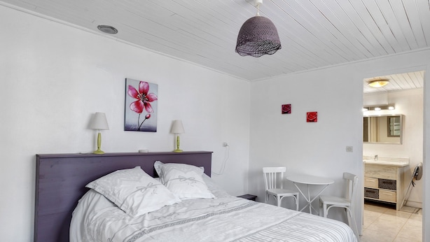 A bedroom with a bed, two bedside lamps, a painting of a flower, a small table, and a chair.