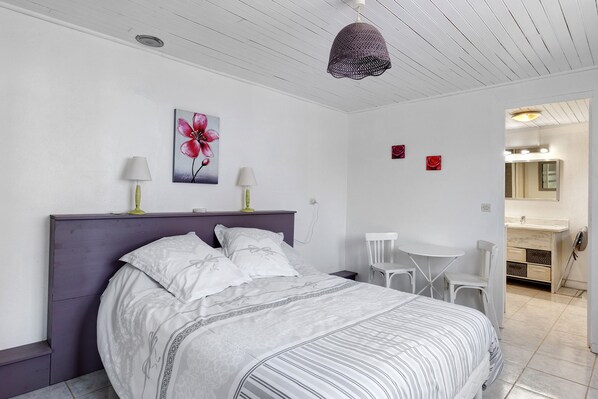 A bedroom with a bed, two bedside lamps, a painting of a flower, a small table, and a chair.
