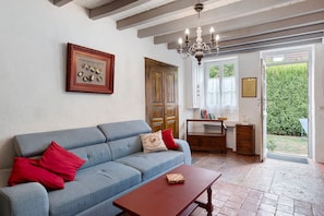 Una stanza con un divano blu, un tavolo di legno, un lampadario e una porta che dà sull'esterno.