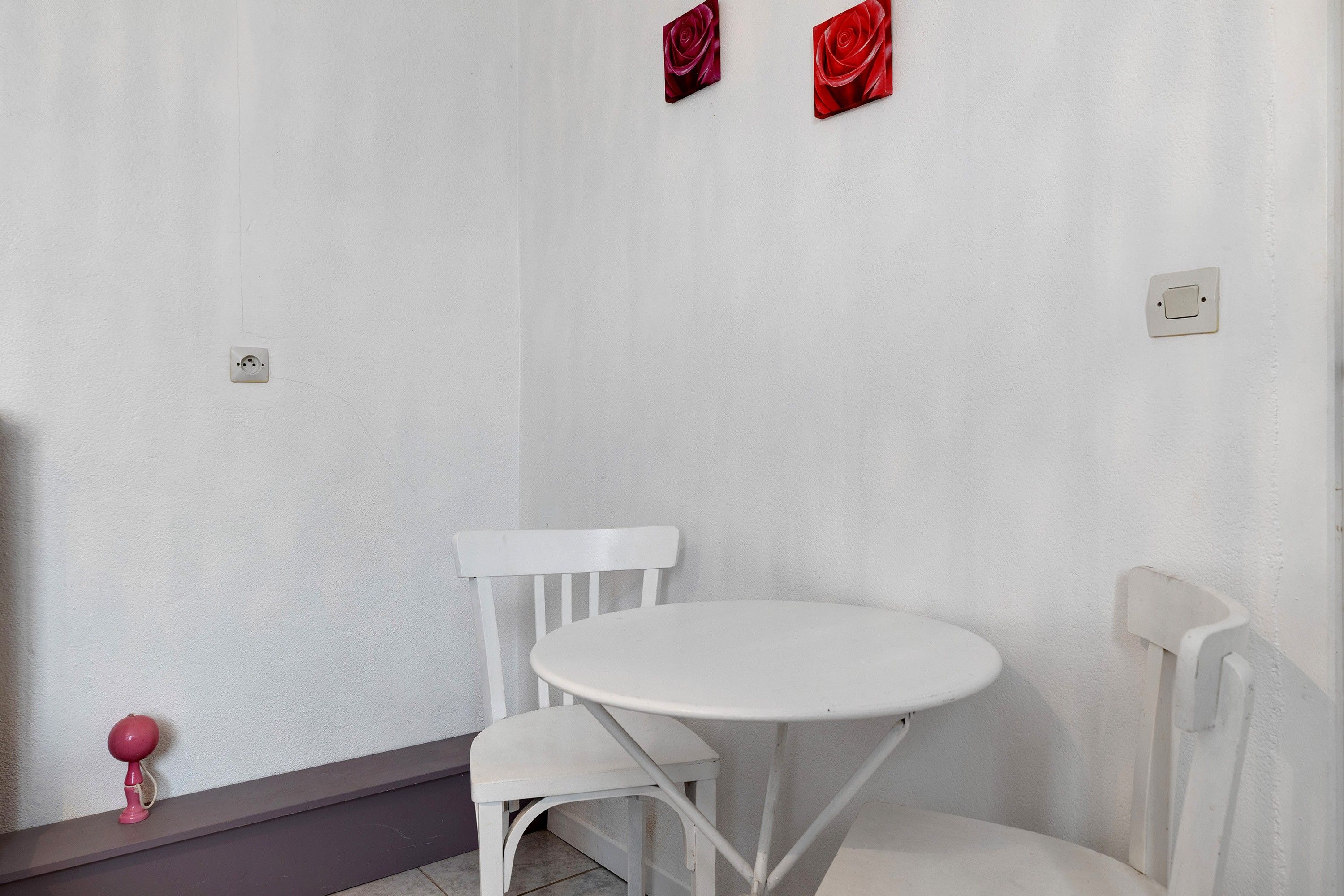 Een witte tafel en stoel in een hoek, tegen een effen muur met een stopcontact.