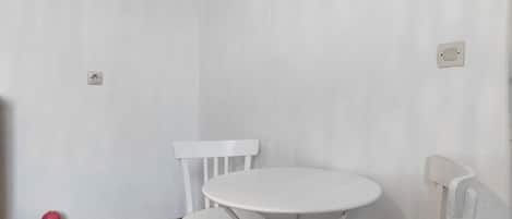 A white table and chair in a corner with a plain wall and a power outlet.