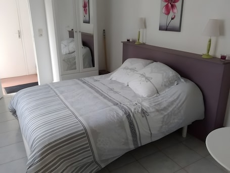 A neatly made bed with a striped bedspread, a headboard, and a bedside table with a lamp.. Guest Room “Le Four à Pains - Charlotte” with Terrace, Garden and Wi-Fi