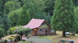 A log cabin with a red roof, surrounded by dense forest. - Historic 1896 Cabin Retreat on 70-Acre Private Forest (Raymond)