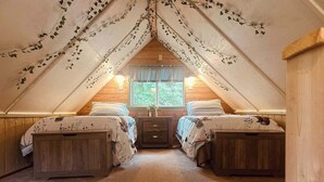 An attic bedroom with two beds, wooden walls, a window with curtains, and ivy decorations. - Historic 1896 Cabin Retreat on 70-Acre Private Forest (Raymond)