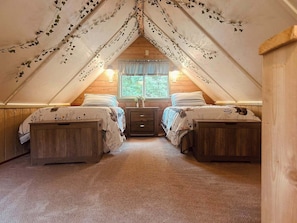 An attic bedroom with two beds, wooden walls, a window with curtains, and ivy decorations.