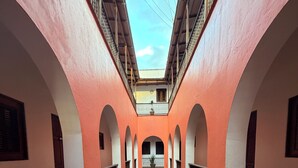 Une cour intérieure agrémentée d’arcades, d’une fontaine centrale et de plantes en pot.