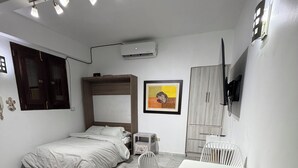 Une chambre à coucher avec un lit, un bureau avec des chaises, une télévision et un tableau accroché au mur.