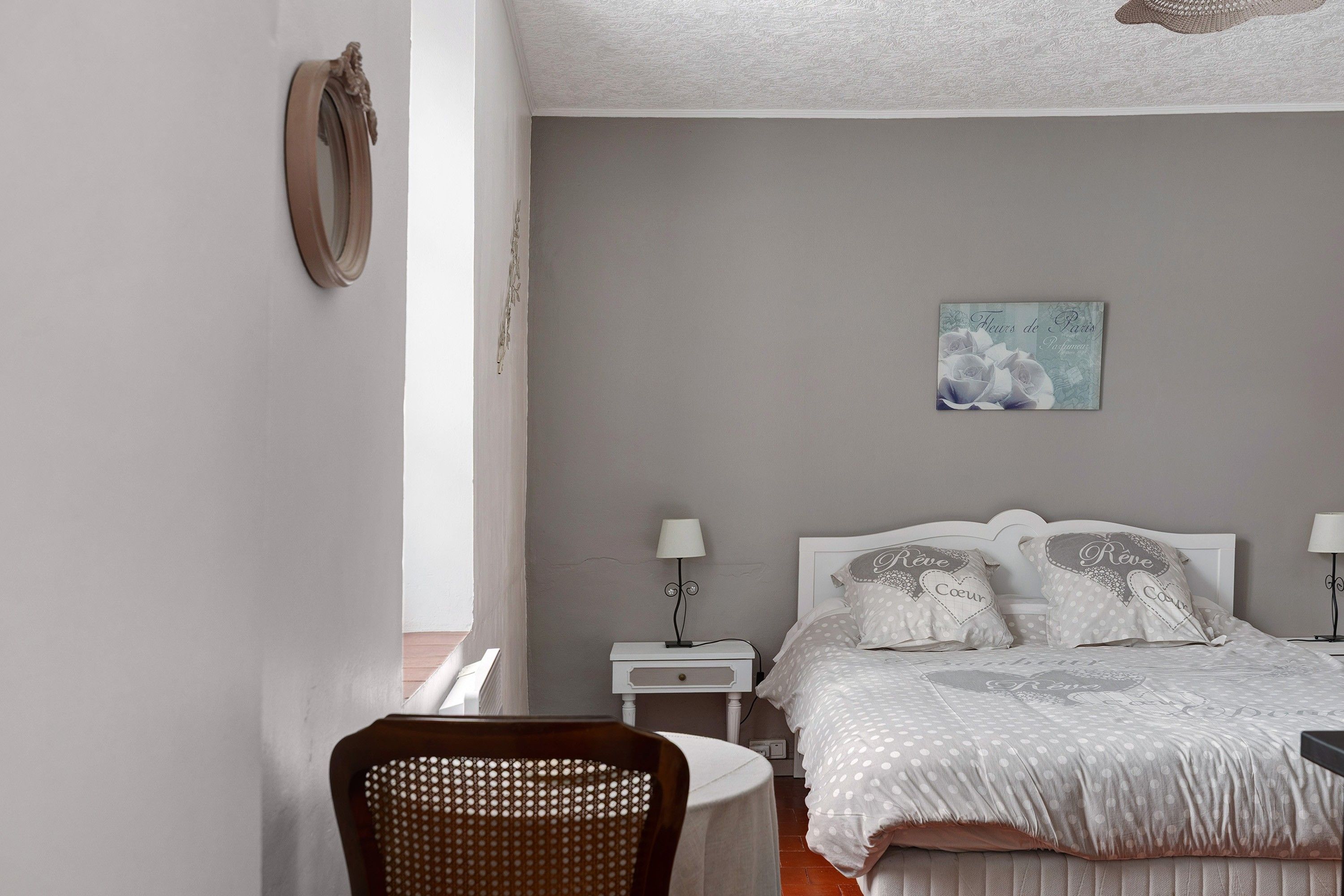 Een slaapkamer met een bed, twee nachtkastjes, een stoel en een aan de muur bevestigd schilderij.