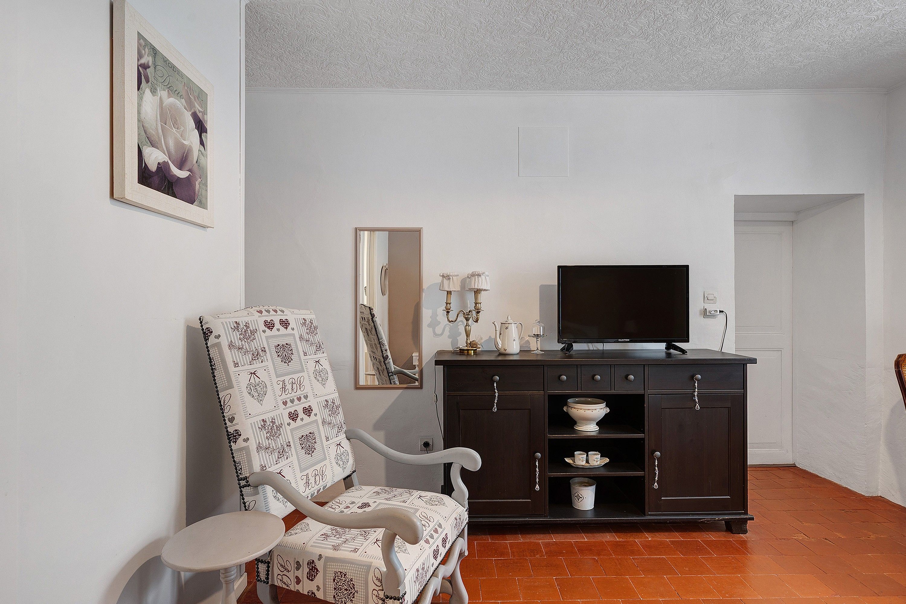 Een woonkamer met een donker houten kast, een televisie, een witte fauteuil en een klein tafeltje.