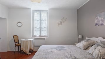 Una camera da letto con un letto, una sedia, un tavolo, una finestra e un elemento decorativo a parete.