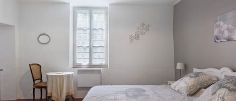 A bedroom with a bed, a chair, a table, a window, and a wall decoration.