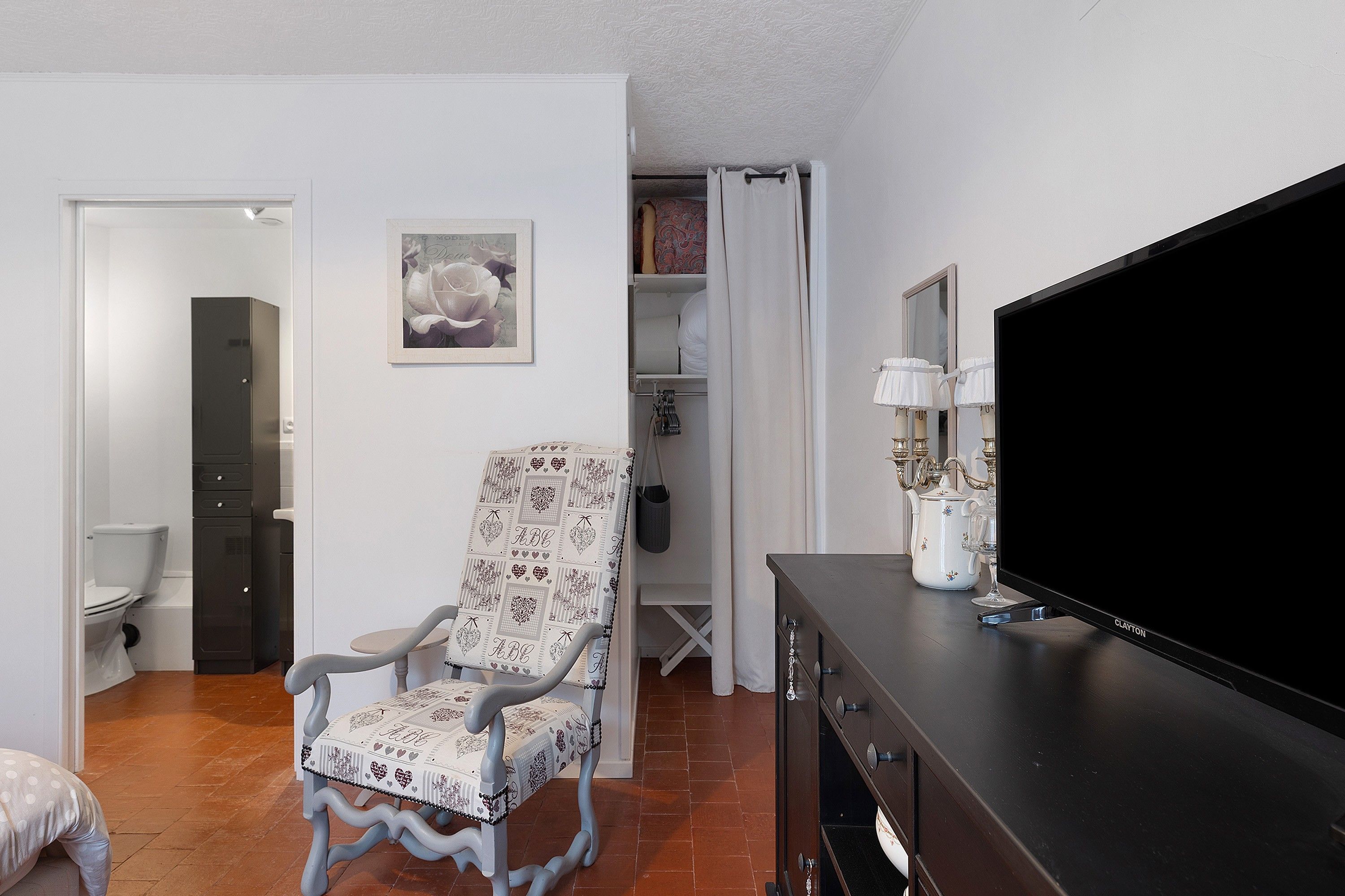 Een woonkamer met een televisie, een gestreept fauteuil, een kast en een deur naar een andere kamer.