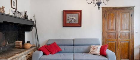 A room with a grey sofa, a red table, a fireplace, a chandelier, and a wooden door.