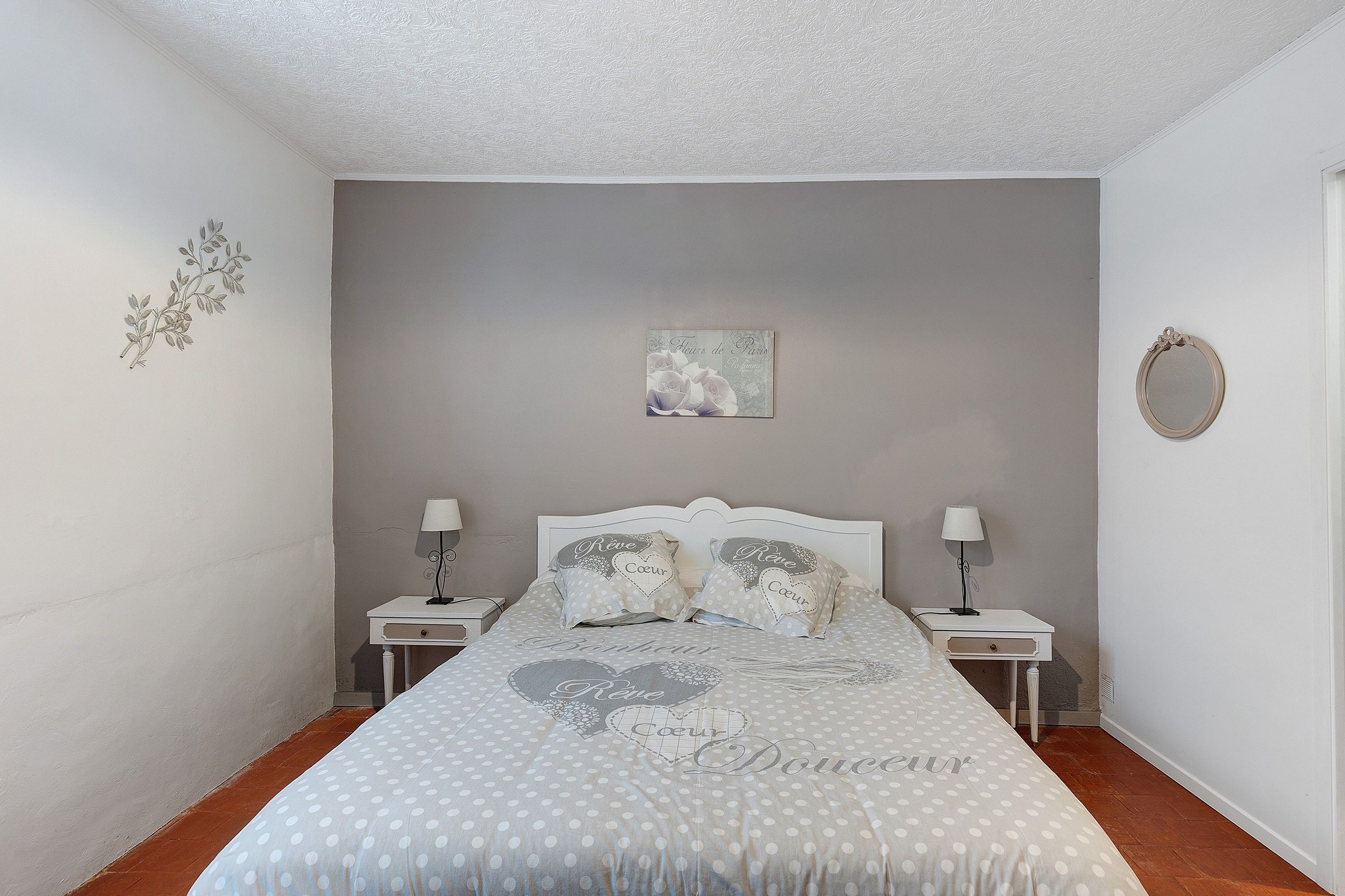 Een slaapkamer met een bed, twee nachtkastjes, een wandspiegel en een decoratief kunstwerk aan de muur.