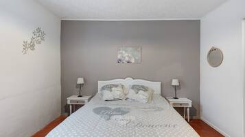 Une chambre à coucher comprenant un lit, deux tables de chevet, une commode, un miroir fixé au mur et un élément décoratif mural.
