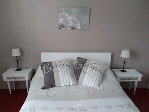 Un lit bien fait, avec des oreillers Ă©tiquetĂ©s « Ă©lĂ©gant », deux tables de chevet avec des lampes et une Ćuvre dâart accrochĂ©e au mur.