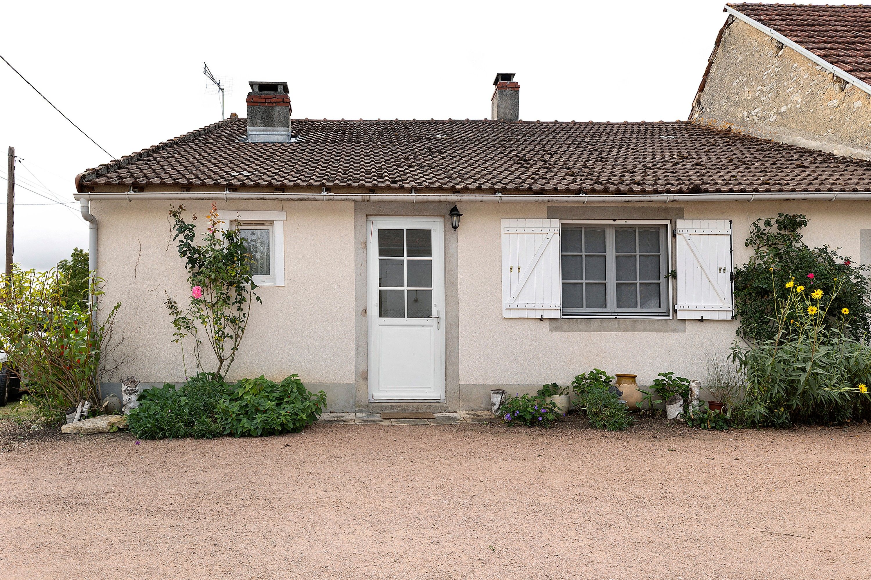 Een huis met één verdieping, voorzien van dakpannen, een witte deur en een raam met luiken.