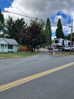 A residential street with a house, a large tree, and a white RV parked on the side.