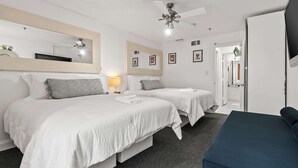 Una habitación de hotel con dos camas, un ventilador de techo, un espejo grande y un televisor.