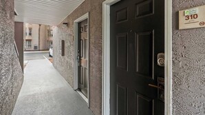 Un pasillo con una puerta oscura, un cartel que indica la habitación 310 y un edificio al fondo.