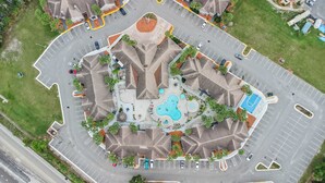Vista aérea de un hotel con piscina central, varios estacionamientos y zonas verdes circundantes.