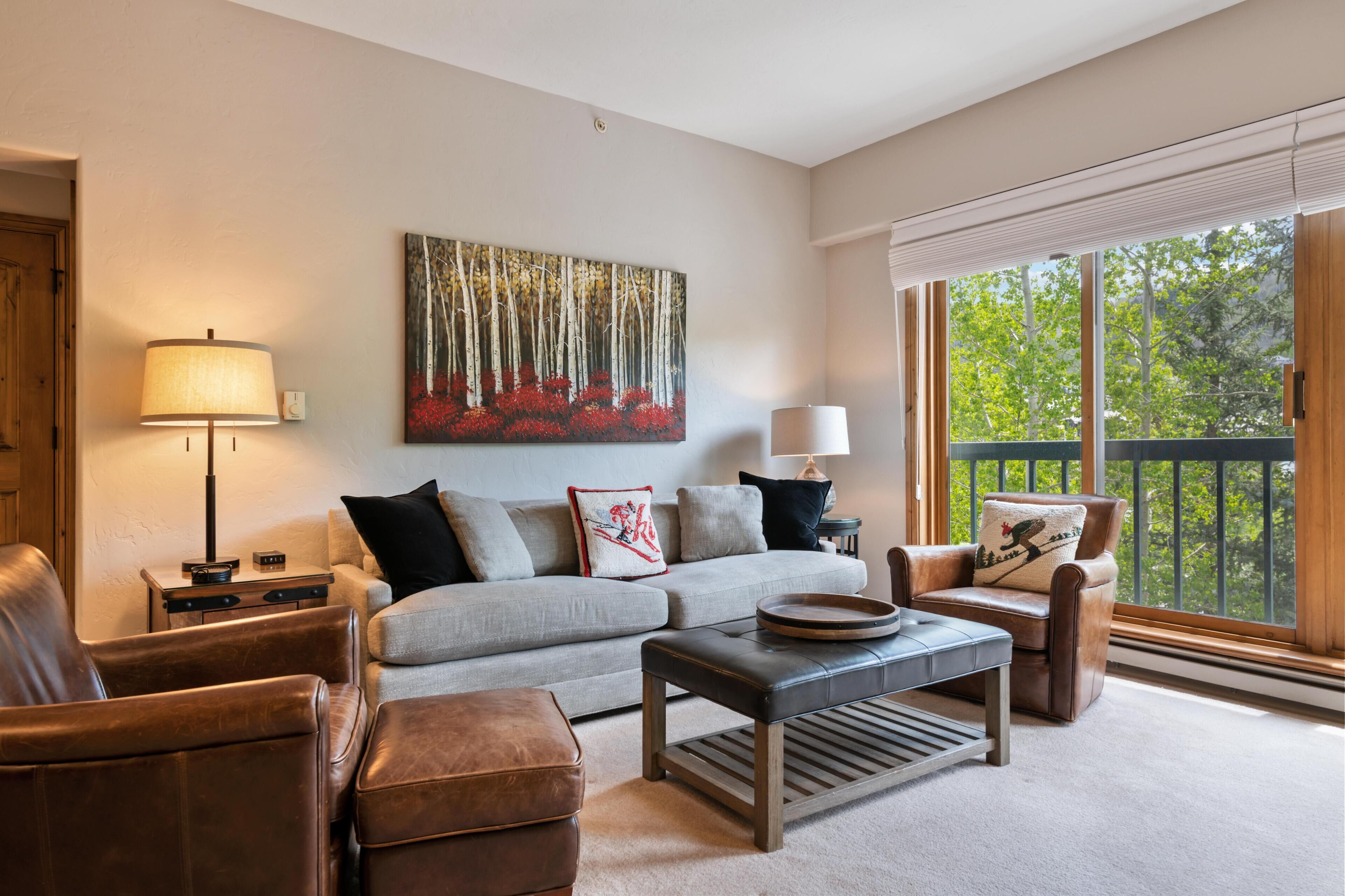 Een woonkamer met een bank, twee fauteuils, een salontafel en een schilderij aan de muur.