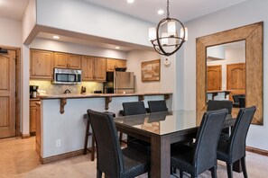 A modern kitchen with wooden cabinets, a stainless steel microwave, and a dining area with a glass table and wicker chairs. - Borders Lodge U308 3BD Beaver Creek Ski-in, Ski-out Condo (Avon)