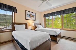 Ein Schlafzimmer mit zwei Betten, einem Deckenventilator und großen Fenstern mit schwarzen Vorhängen.