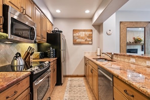 A kitchen with wooden cabinets, stainless steel appliances, a granite countertop, and a patterned rug. - Borders Lodge U308 3BD Beaver Creek Ski-in, Ski-out Condo (Avon)