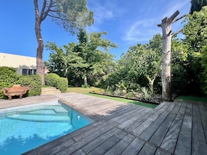 Une terrasse en bois, une piscine et une variété de plantes, notamment des arbres et des arbustes.