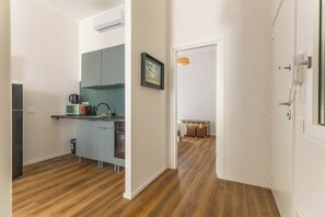 Une cuisine moderne équipée d’un four à micro-ondes, d’une bouilloire et de placards, donnant sur une salle de bain avec douche et un espace pour ranger une valise.