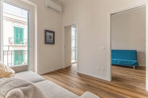 Um quarto com piso de madeira, um sofá, uma cama com cobertura azul e uma varanda com persianas verdes.
