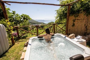 Eine Person entspannt sich in einem Whirlpool mit Blick auf Berge und ein Gewässer.