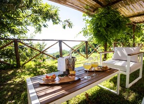 Ein Holztisch mit Speisen und Getränken, ein weißer Stuhl und Blick auf Grünflächen und Hügel.