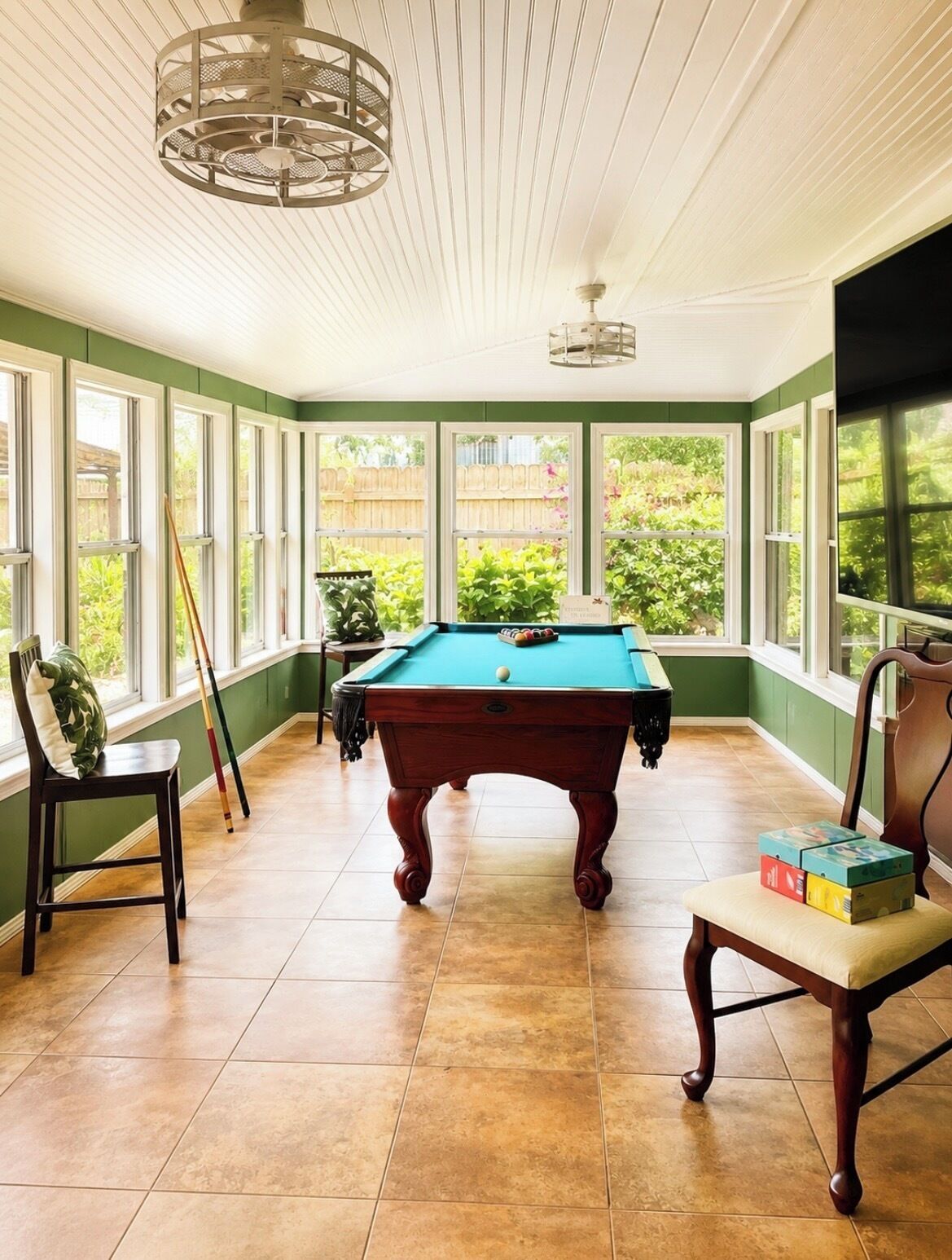 A pool table in a room with large windows, a ceiling fan, and a view of greenery outside.