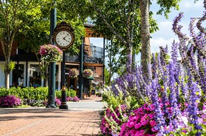 A street with a clock, flowers, and a building with a balcony.