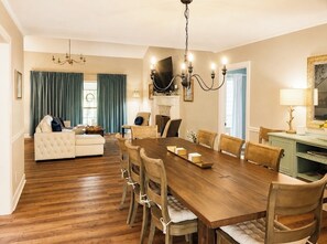 A dining area with a wooden table, chairs, a chandelier, and a sofa. - Grand Oak Cottage in Olde Town, 2 King Primary Suites, year round Saltwater Pool (Daphne)