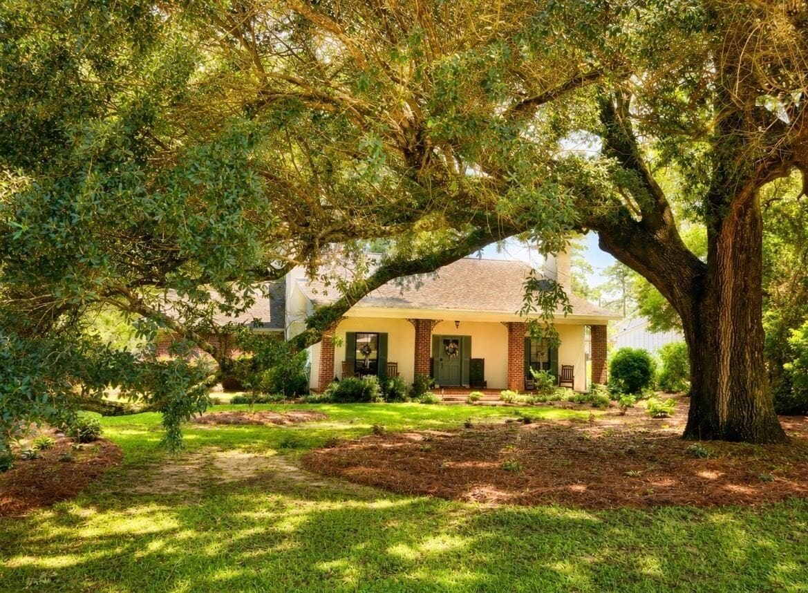 A house with a large tree in front, a well-maintained lawn, and a brick exterior.