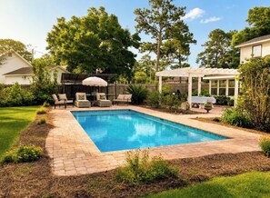 A backyard with a rectangular swimming pool, a covered patio area, and a seating arrangement.